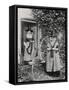 Two Welshwomen in Traditional Dress Stand Outside Their Cottage with a Spinning Wheel-null-Framed Stretched Canvas