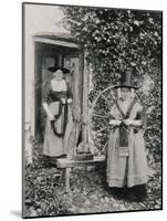Two Welshwomen in Traditional Dress Stand Outside Their Cottage with a Spinning Wheel-null-Mounted Photographic Print