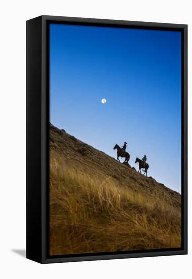 Two wranglers riding horses up a hill with full moon in background at blue hour-Sheila Haddad-Framed Stretched Canvas