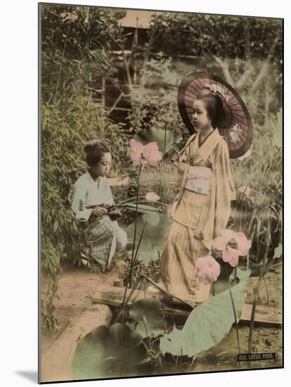 Two Young Japanese Girls, One Holding a Parasol, with Lotus Flowers-null-Mounted Photographic Print