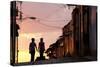 Two Young People in Silhouette at Sunset on Cobbled Street with Colourful Orange Sky Behind-Lee Frost-Stretched Canvas