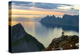 Two young women watching sunset standing on mountain top, Senja island, Troms county-Roberto Moiola-Stretched Canvas