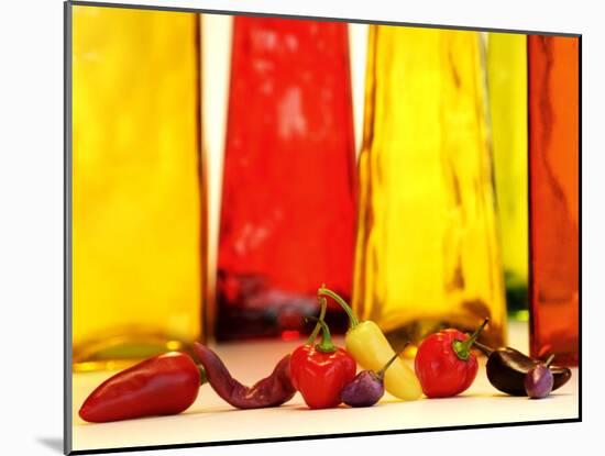 Various Types of Peppers in Front of Red & Yellow Bottles-Monica Varella-Mounted Photographic Print