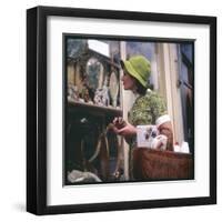 Woman in a Green Floppy Hat and Green Dress Browses in a Shop Selling Various Mirrors and Ornaments-null-Framed Art Print