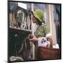 Woman in a Green Floppy Hat and Green Dress Browses in a Shop Selling Various Mirrors and Ornaments-null-Mounted Art Print