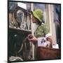 Woman in a Green Floppy Hat and Green Dress Browses in a Shop Selling Various Mirrors and Ornaments-null-Mounted Art Print