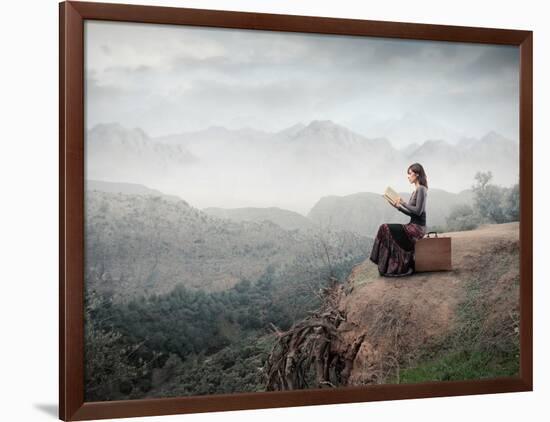 Woman Sitting On A Suitcase And Reading A Book With Landscape On The Background-olly2-Framed Art Print