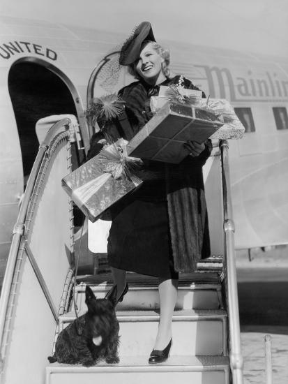 Woman with Gifts Climbing Down Airplane Stairs' Photo