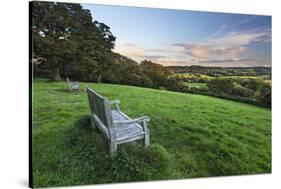 Wooden bench looking over green field countryside of High Weald on summer evening, Burwash-Stuart Black-Stretched Canvas