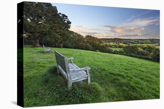 Wooden bench looking over green field countryside of High Weald on summer evening, Burwash-Stuart Black-Stretched Canvas