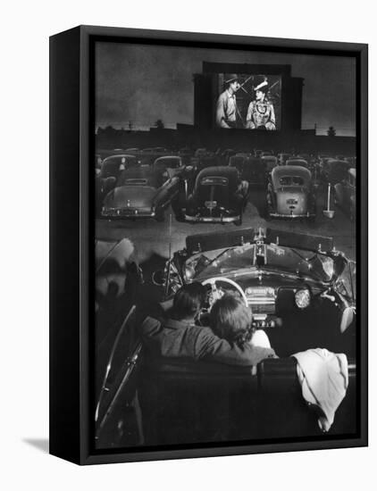 Young Couple Snuggling in Convertible as They Watch Large Screen Action at a Drive-In Movie Theater-J^ R^ Eyerman-Framed Stretched Canvas
