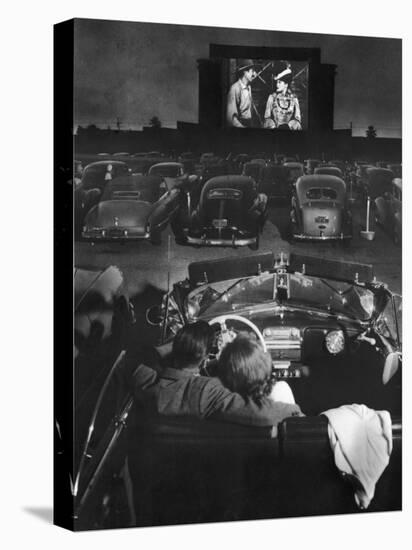 Young Couple Snuggling in Convertible as They Watch Large Screen Action at a Drive-In Movie Theater-J^ R^ Eyerman-Stretched Canvas