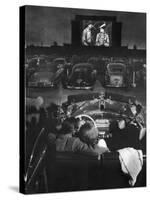 Young Couple Snuggling in Convertible as They Watch Large Screen Action at a Drive-In Movie Theater-J^ R^ Eyerman-Stretched Canvas