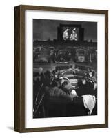 Young Couple Snuggling in Convertible as They Watch Large Screen Action at a Drive-In Movie Theater-J^ R^ Eyerman-Framed Premium Photographic Print