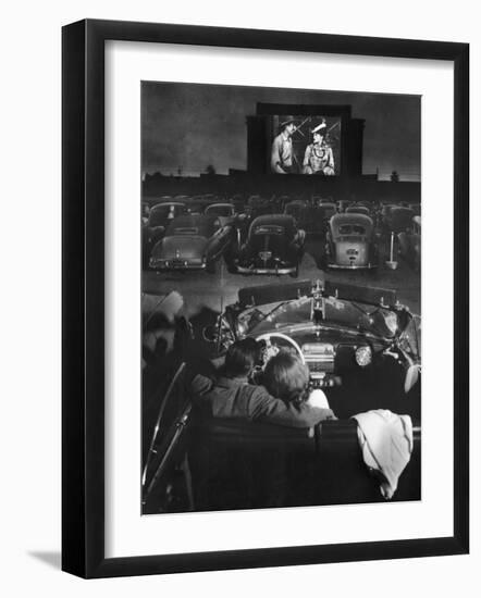 Young Couple Snuggling in Convertible as They Watch Large Screen Action at a Drive-In Movie Theater-J^ R^ Eyerman-Framed Premium Photographic Print