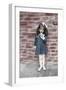 Young Girl Standing in Front of a Stone Wall Smelling a Flower.-Nora Hernandez-Framed Giclee Print