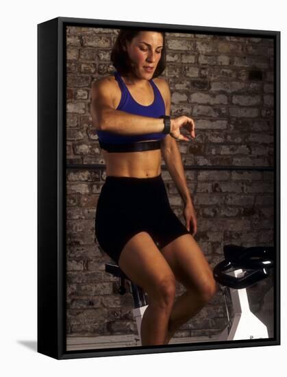 Young Woman Exercising on a Stationary Bike Checking her Heart Rate-null-Framed Stretched Canvas