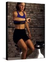 Young Woman Exercising on a Stationary Bike Checking her Heart Rate-null-Stretched Canvas