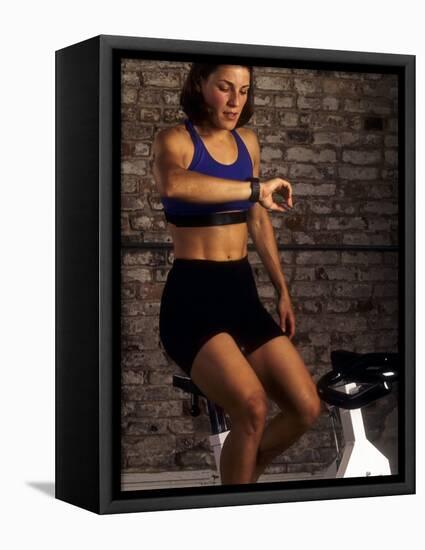 Young Woman Exercising on a Stationary Bike Checking her Heart Rate-null-Framed Stretched Canvas