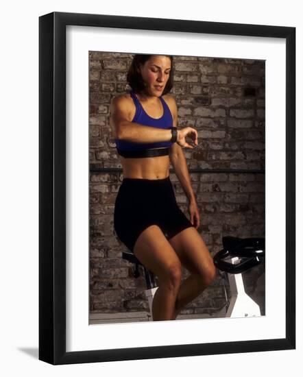 Young Woman Exercising on a Stationary Bike Checking her Heart Rate-null-Framed Photographic Print