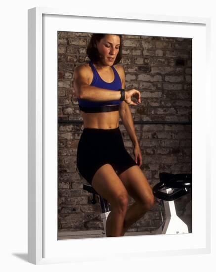 Young Woman Exercising on a Stationary Bike Checking her Heart Rate-null-Framed Photographic Print