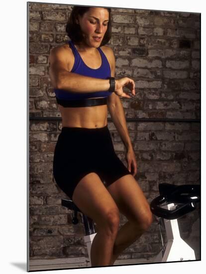 Young Woman Exercising on a Stationary Bike Checking her Heart Rate-null-Mounted Photographic Print