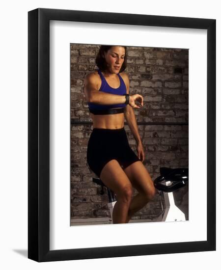 Young Woman Exercising on a Stationary Bike Checking her Heart Rate-null-Framed Photographic Print