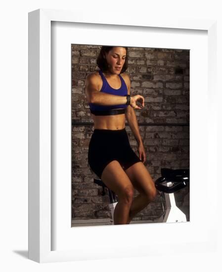 Young Woman Exercising on a Stationary Bike Checking her Heart Rate-null-Framed Photographic Print