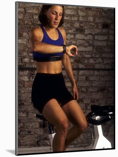 Young Woman Exercising on a Stationary Bike Checking her Heart Rate-null-Mounted Photographic Print