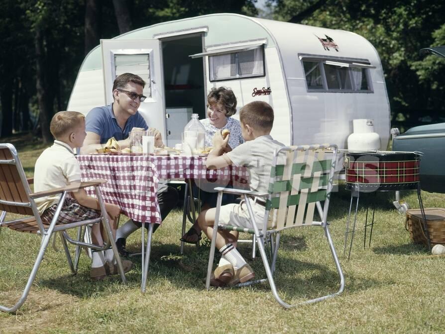 1960s Family Sitting In Lawn Chairs At Picnic Table Beside Camping