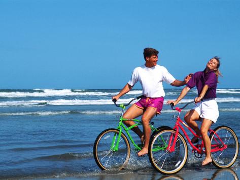 Middle Aged Couple Riding Bikes On The Beach Middle Aged Couple Riding Bikes On The Beach